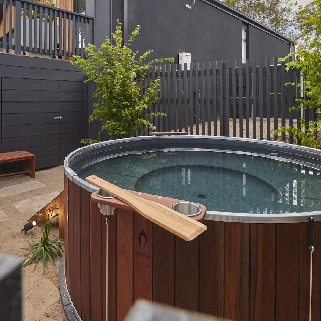 Wooden hot tub with a paddle in a backyard setting.