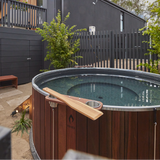 Wooden hot tub with a paddle in a backyard setting.