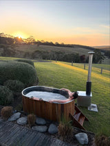 Person relaxing in an outdoor hot tub with a scenic view at sunset.